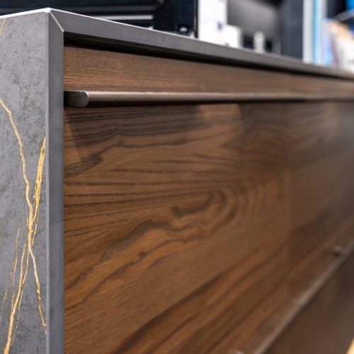 Close up of dark veneer paired with a gray stone panel and gold veining in a showroom setting. A luxury minimalism look for contemporary interiors and design briefs.